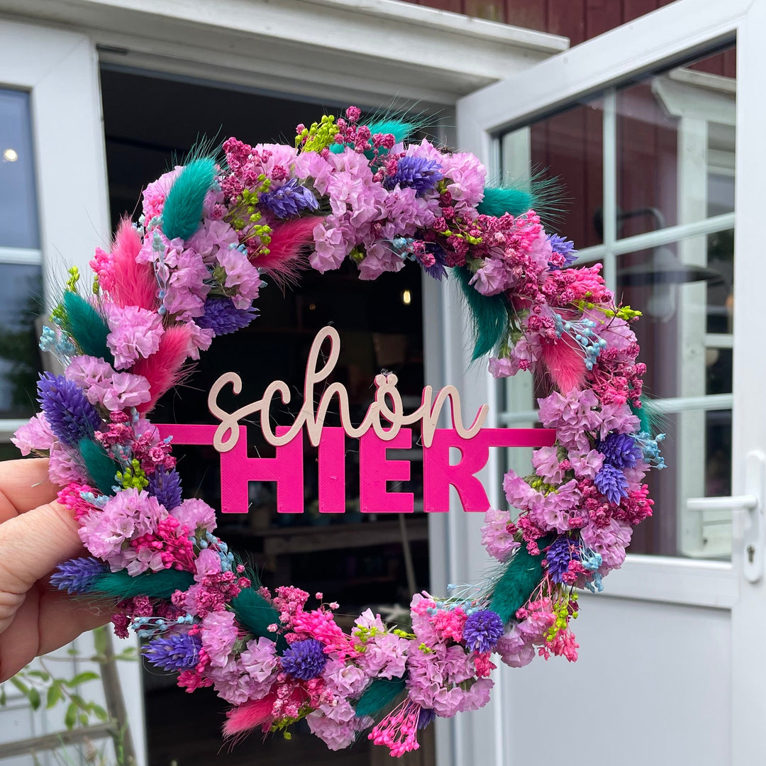 bunter Trockenblumenkranz wird von einer Hand hochgehalten und vor einem Blumenladen präsentiert